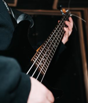 Close-up musician guitarist playing bass guitar strings indoors, selective focus Close-up musician guitarist playing bass guitar strings indoors, selective focus